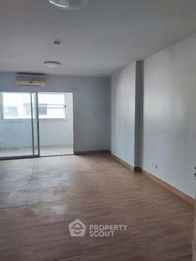 Spacious living room with large window and sliding glass door to balcony, featuring modern flooring.