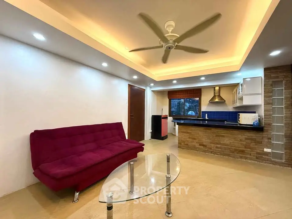 Modern living room with stylish ceiling fan, cozy red sofa, and sleek open kitchen design.