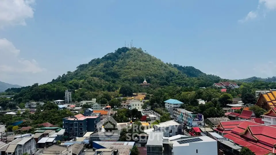 Scenic view of a vibrant town nestled at the base of a lush green hill under a clear blue sky.