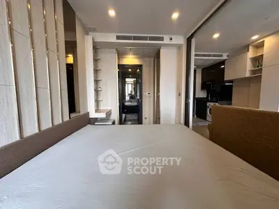 Modern bedroom with sleek design and open kitchen view, featuring neutral tones and contemporary furnishings.
