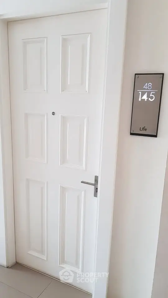 Modern apartment entrance with sleek white door and stylish room number plaque.