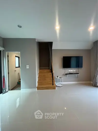 Modern living room with sleek staircase and wall-mounted TV, featuring elegant lighting and glossy tiled flooring.