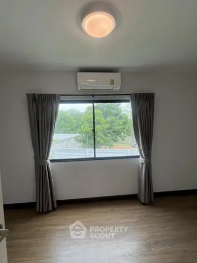 Bright bedroom with large window and air conditioning, featuring elegant curtains and wooden flooring.