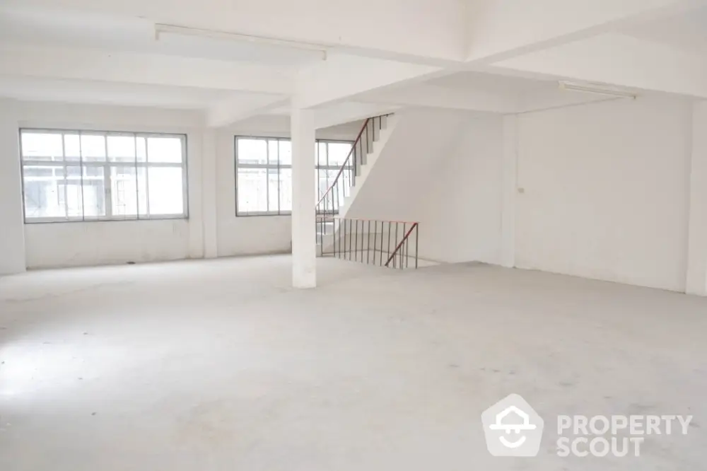 Spacious and bright open-plan interior with large windows and a staircase, ideal for a modern living space or creative studio.