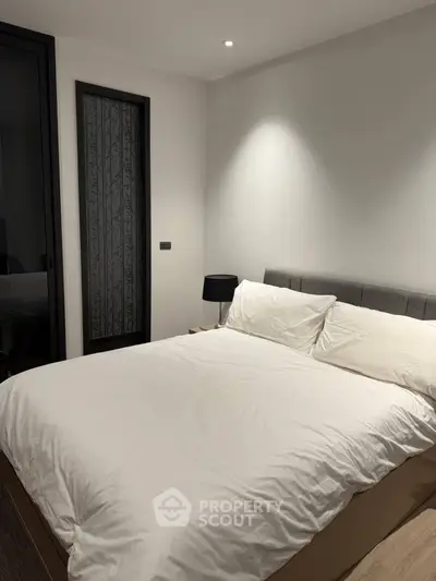 Modern bedroom with cozy lighting and elegant decor, featuring a comfortable bed and stylish bedside lamp.