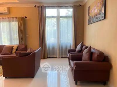 Spacious living room with elegant brown leather sofas and large windows for natural light.