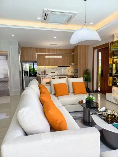 Luxurious open-plan living room with modern kitchen, featuring elegant decor and vibrant orange accents.