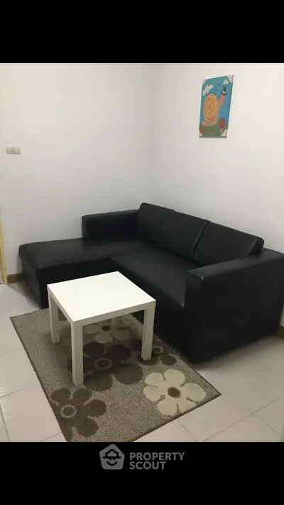 Cozy living room with black sofa and white coffee table on floral rug.