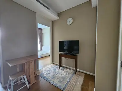 Cozy living area with TV and wooden furniture, leading to a bedroom with natural light.