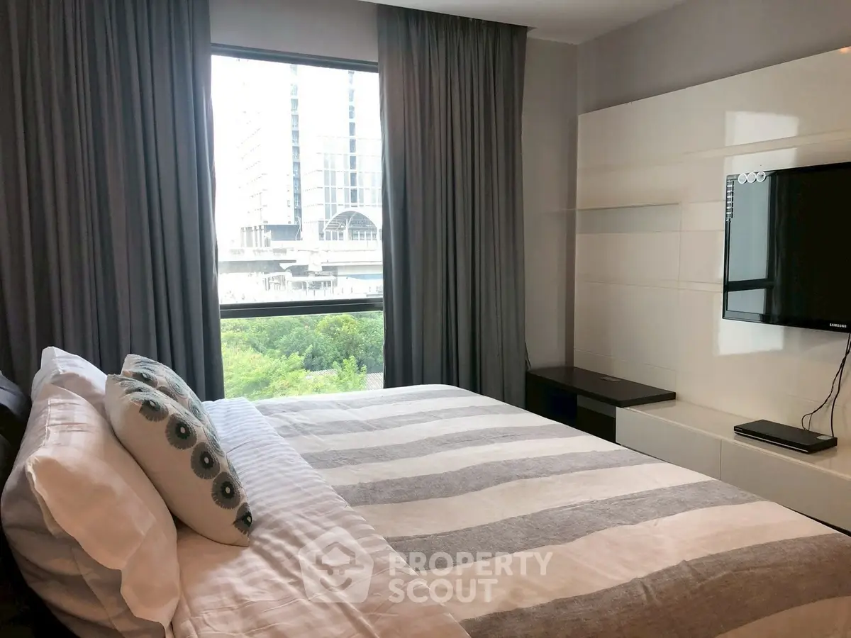 Modern bedroom with large window and stylish decor in urban apartment.