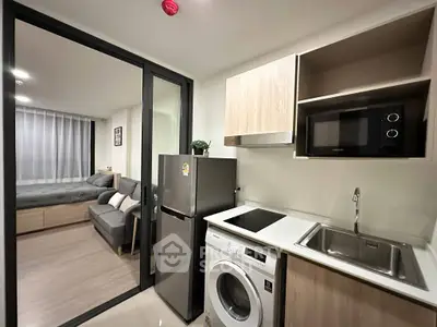 Modern apartment kitchen with washing machine and microwave, open layout to cozy living room.