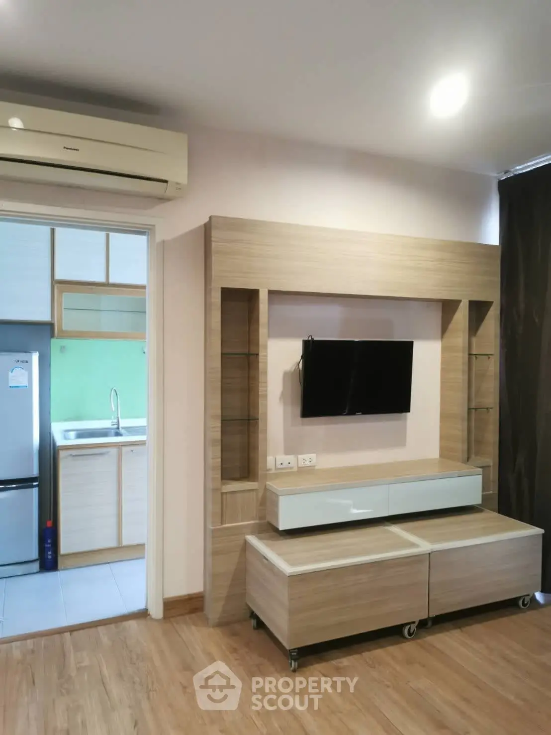 Modern living room with wooden flooring and sleek TV unit, adjacent to a compact kitchen.
