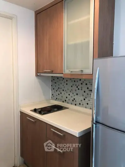 Compact kitchen with modern cabinetry and mosaic backsplash, featuring a sleek electric cooktop and stainless steel fridge.