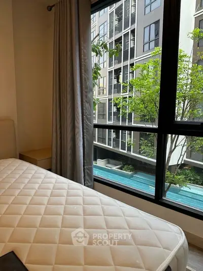 Modern bedroom with large window overlooking pool and greenery in urban setting.
