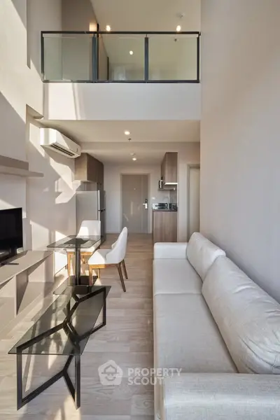 Modern living room with high ceiling and mezzanine, featuring sleek furniture and natural light.