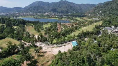 Scenic aerial view of lush green landscape with mountains and lake, ideal for real estate development.