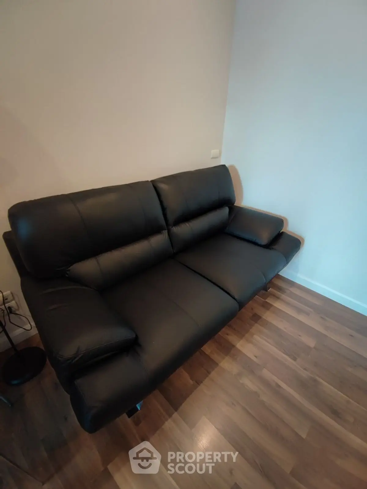 Modern black leather sofa in a cozy living room with wooden flooring.