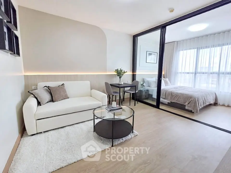 Modern studio apartment with stylish living area and cozy bedroom separated by glass partition.