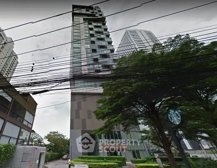 Modern high-rise building with unique facade and lush greenery in urban setting.