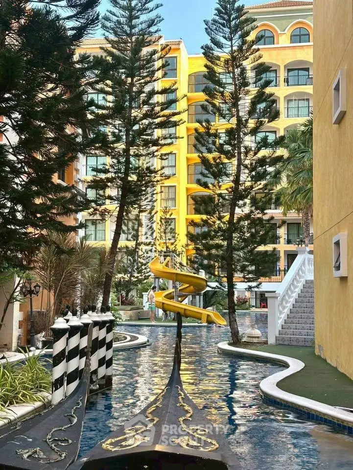 Luxurious apartment complex with unique water feature and slide, surrounded by lush greenery.