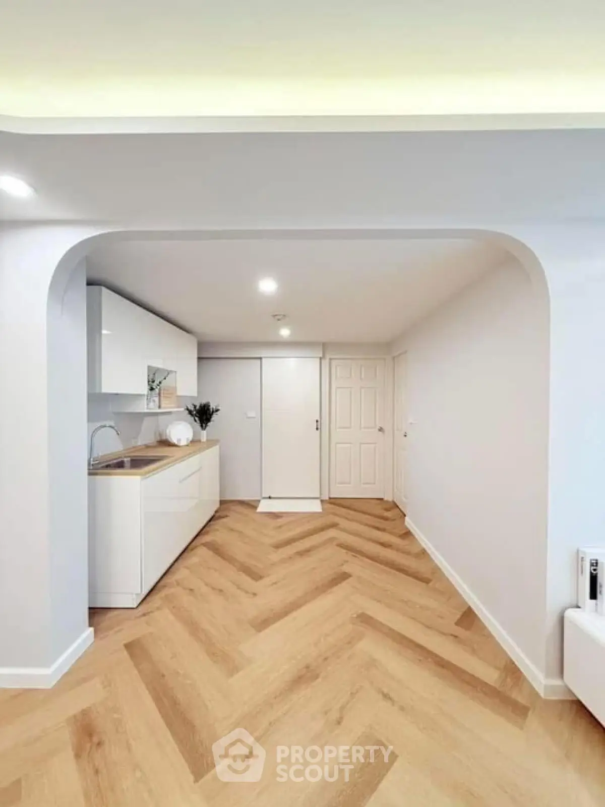 Modern minimalist kitchen with herringbone wood flooring and sleek white cabinetry.