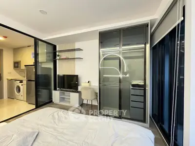 Modern bedroom with sleek wardrobe and compact study area, adjacent to a kitchen with appliances.