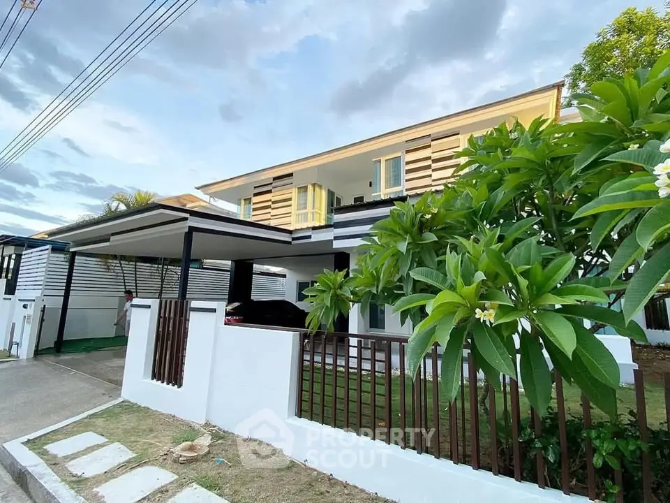 Modern two-story house with carport and lush garden in a serene neighborhood.