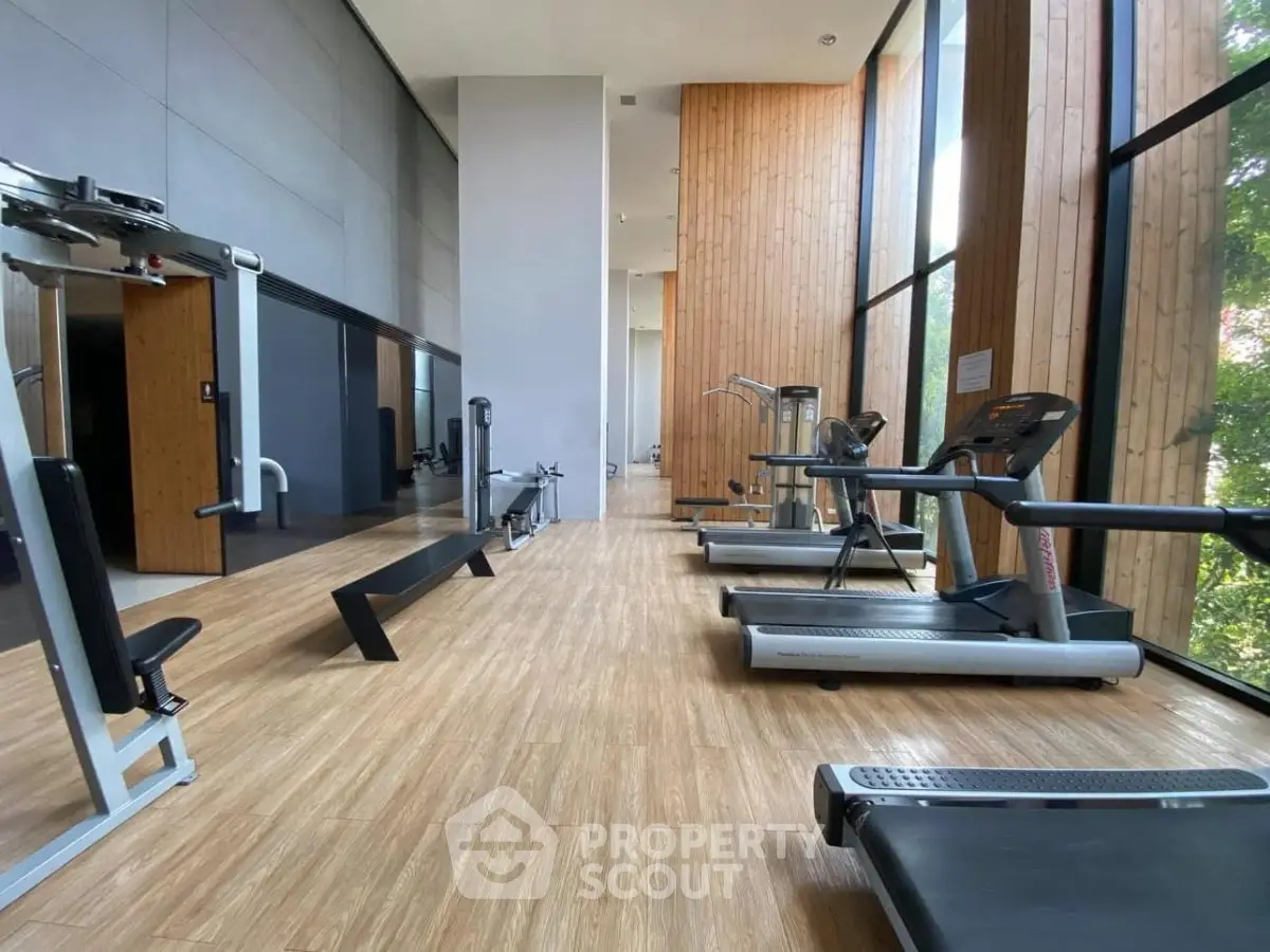Spacious modern gym with large windows and state-of-the-art equipment in luxury building.