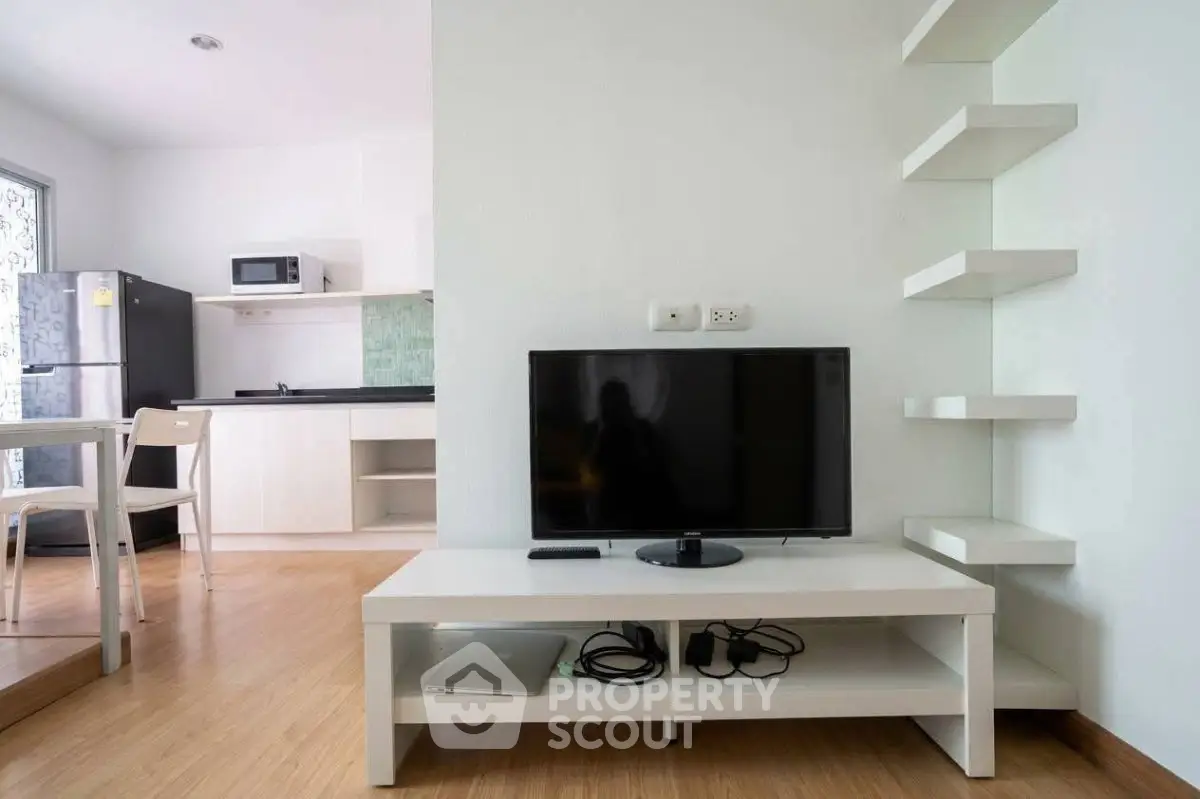 Modern living room with sleek TV setup and minimalist kitchen in open layout apartment.