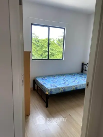 Cozy bedroom with single bed and window view of lush greenery.