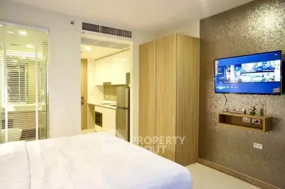 Modern bedroom with sleek TV setup and view into compact kitchen area