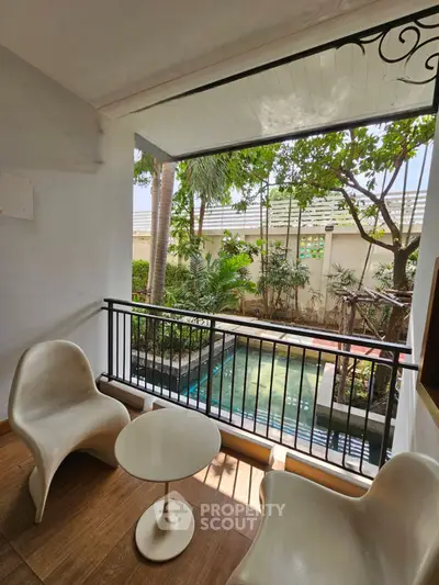 Charming balcony with pool view and modern seating in lush garden setting.