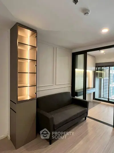 Modern living room with sleek sofa and illuminated display cabinet, featuring sliding glass doors to balcony.