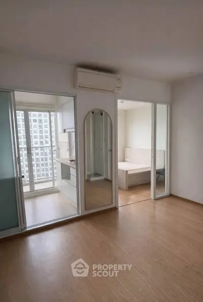 Modern apartment with wooden flooring and glass partitions, featuring a compact kitchen and bedroom.