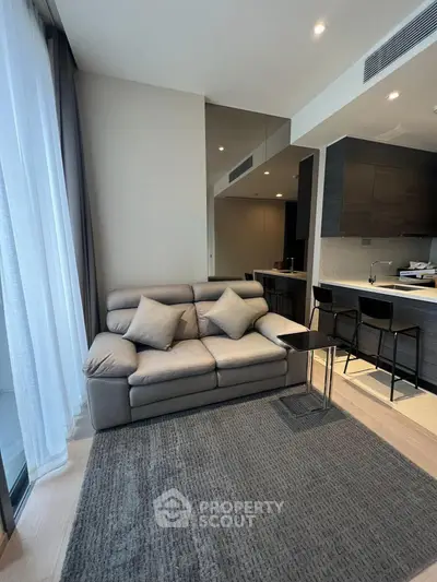Modern living room with sleek design and open kitchen layout, featuring a cozy sofa and stylish bar seating.