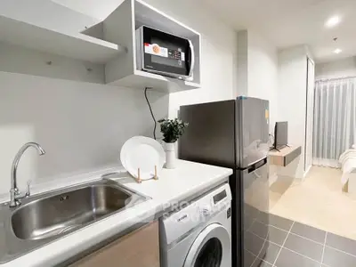 Modern kitchen with sleek appliances and cozy living area in open layout apartment.