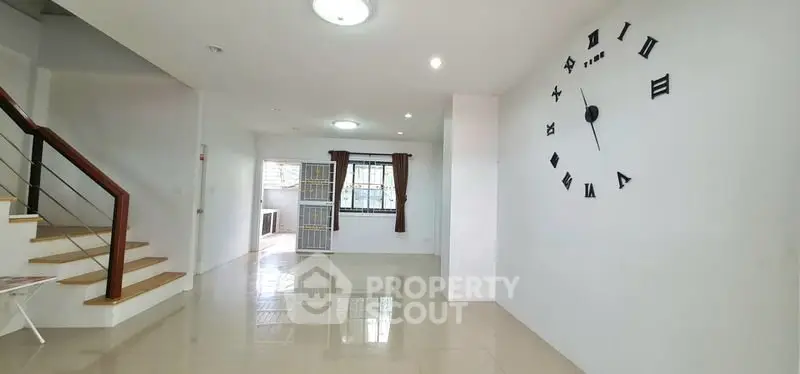 Spacious modern living room with unique wall clock and elegant staircase in a bright home.