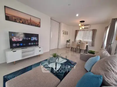 Modern living room with stylish decor and large TV, open to dining area, featuring cozy seating and elegant lighting.