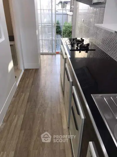 Modern kitchen with sleek design and gas stove, featuring natural light and wooden flooring.