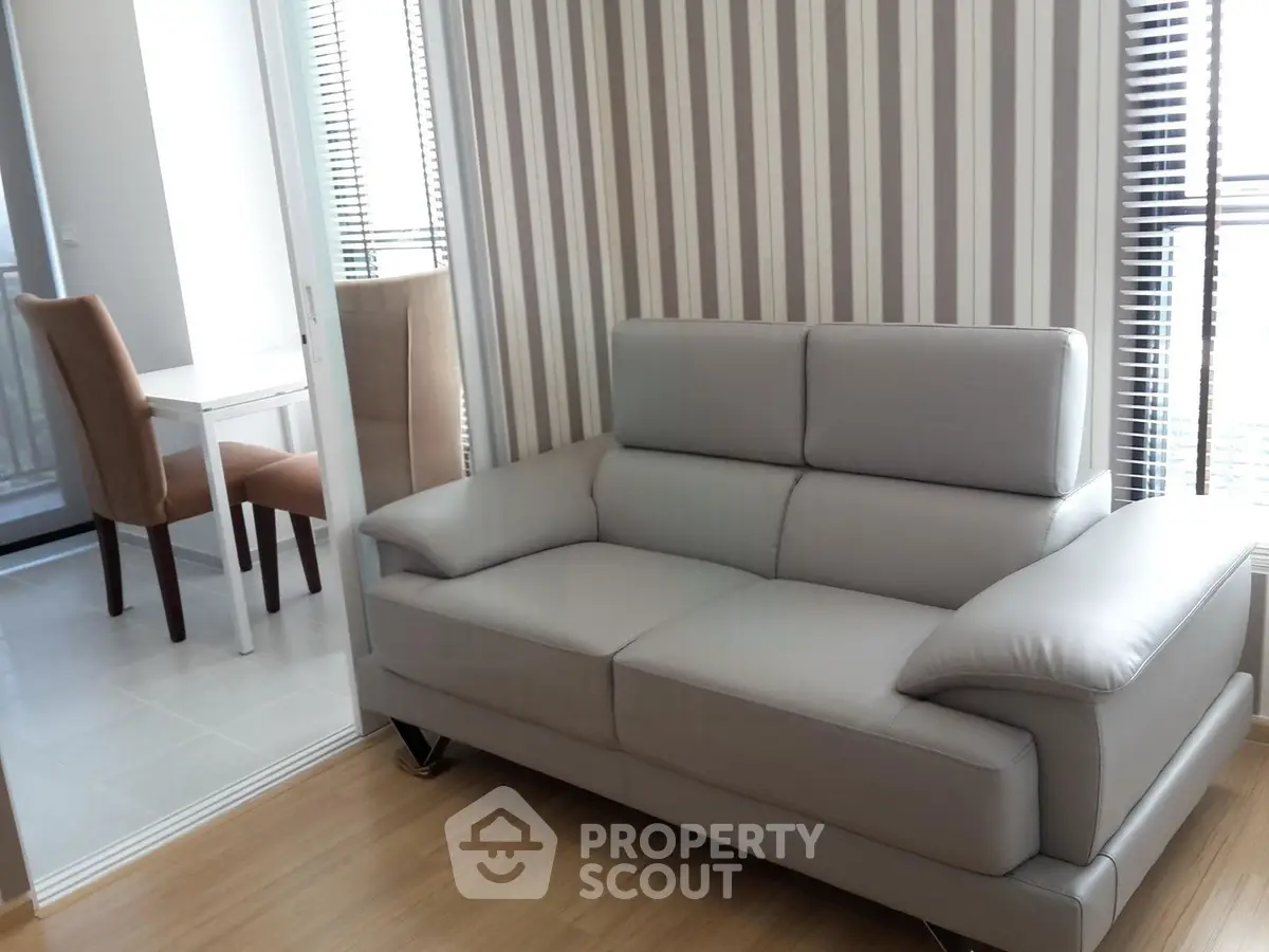 Modern living room with sleek gray sofa and striped wallpaper, adjacent to a dining area with natural light.
