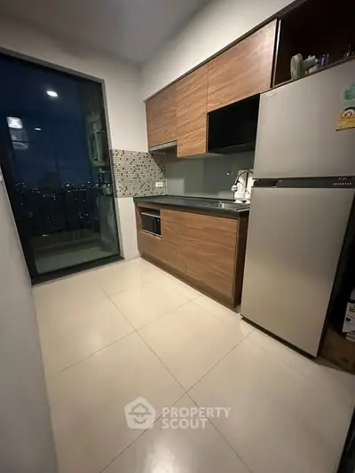 Modern kitchen with sleek cabinets and stainless steel fridge, offering a cozy cooking space with city view.