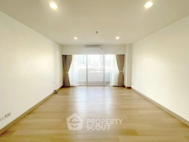 Spacious empty living room with large windows and wooden flooring, perfect for customization.