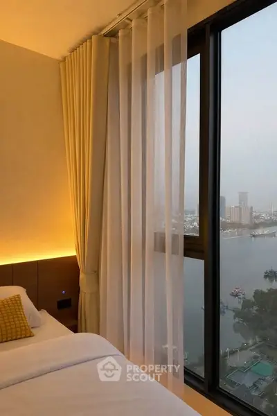 Luxurious bedroom with stunning river view through large window, elegant curtains, and cozy bedding.