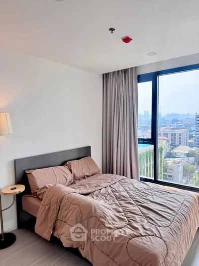 Modern bedroom with city view, featuring a cozy bed and large window for natural light.