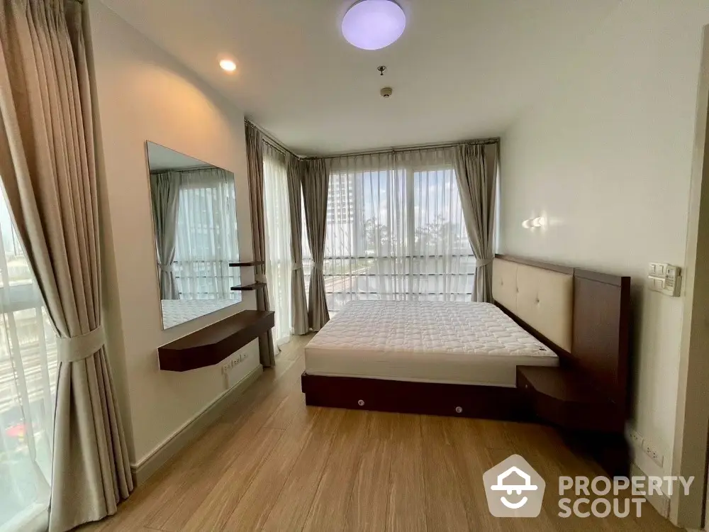 Spacious bedroom with large windows and modern furnishings in a high-rise apartment.