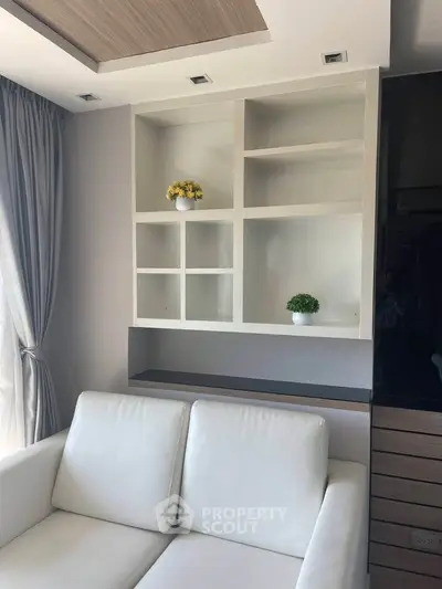 Modern living room with white sofa and built-in shelving, featuring natural light and elegant decor.