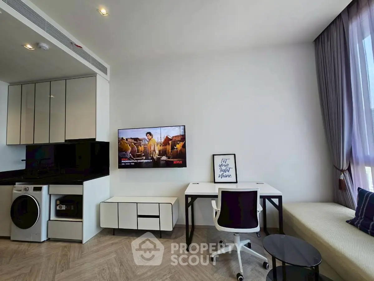 Modern living room with sleek furniture, wall-mounted TV, and compact kitchen area.