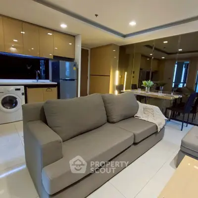 Modern living room with open kitchen, featuring sleek appliances and cozy seating area.