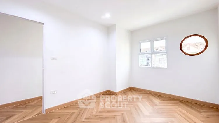 Bright empty room with herringbone wood flooring and unique round window