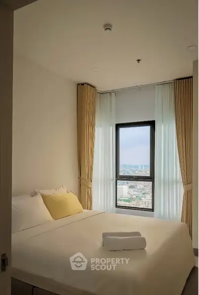 Cozy bedroom with city view, featuring a large window and elegant curtains.